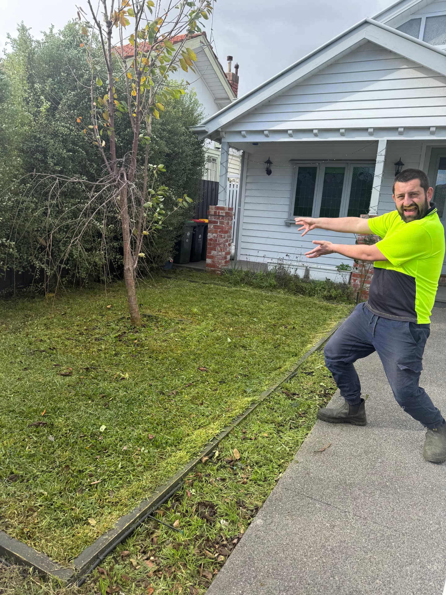 A worker in a hi-vis shirt standing proudly beside a freshly mowed front lawn